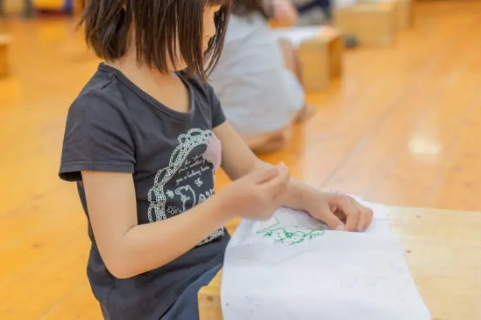 針と糸で布にぬいつけている子どもたち