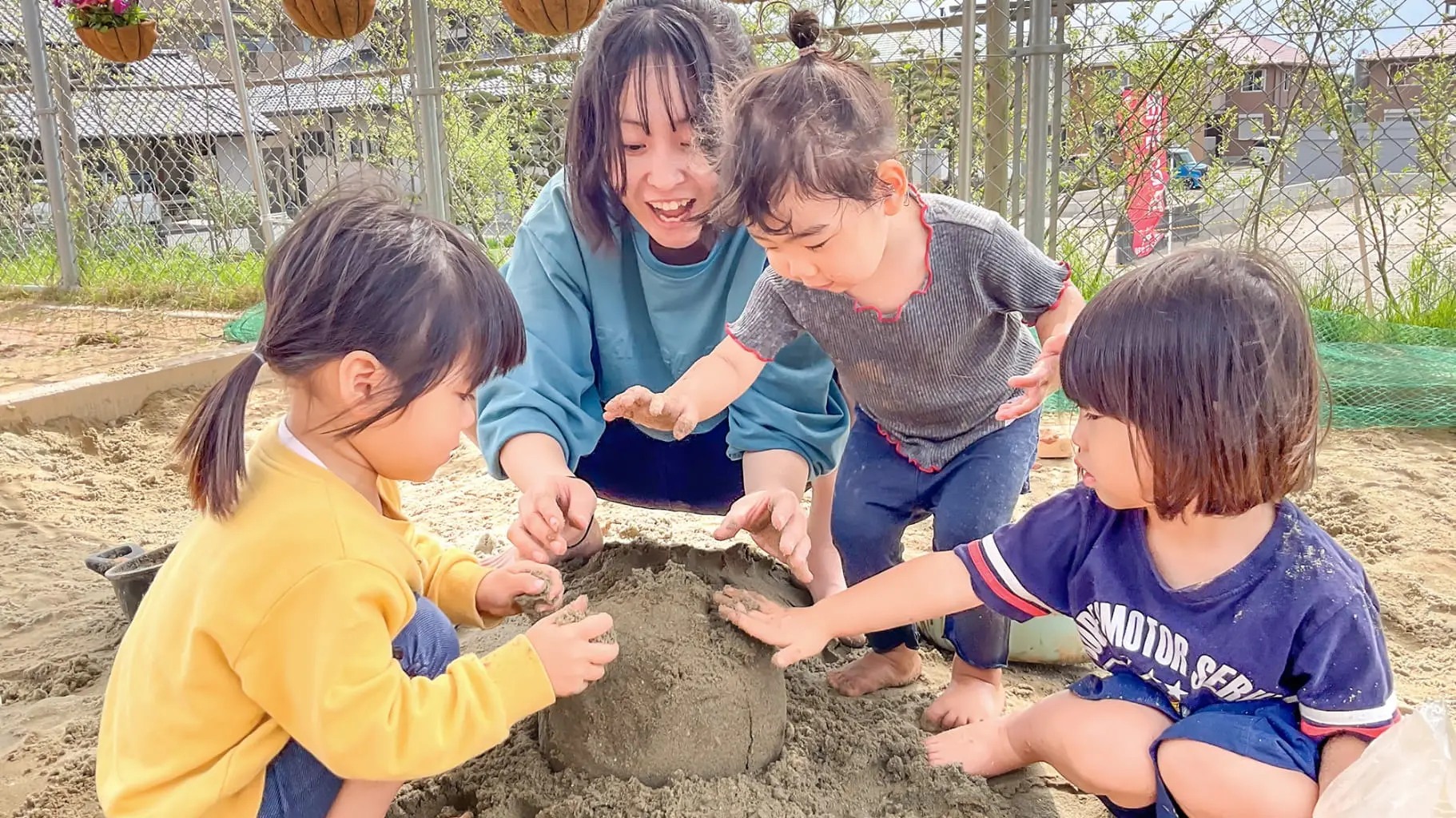 砂場で遊ぶ教諭と子どもたち