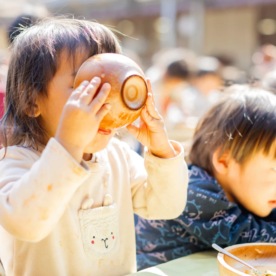 外で汁椀を持って食事をする子ども