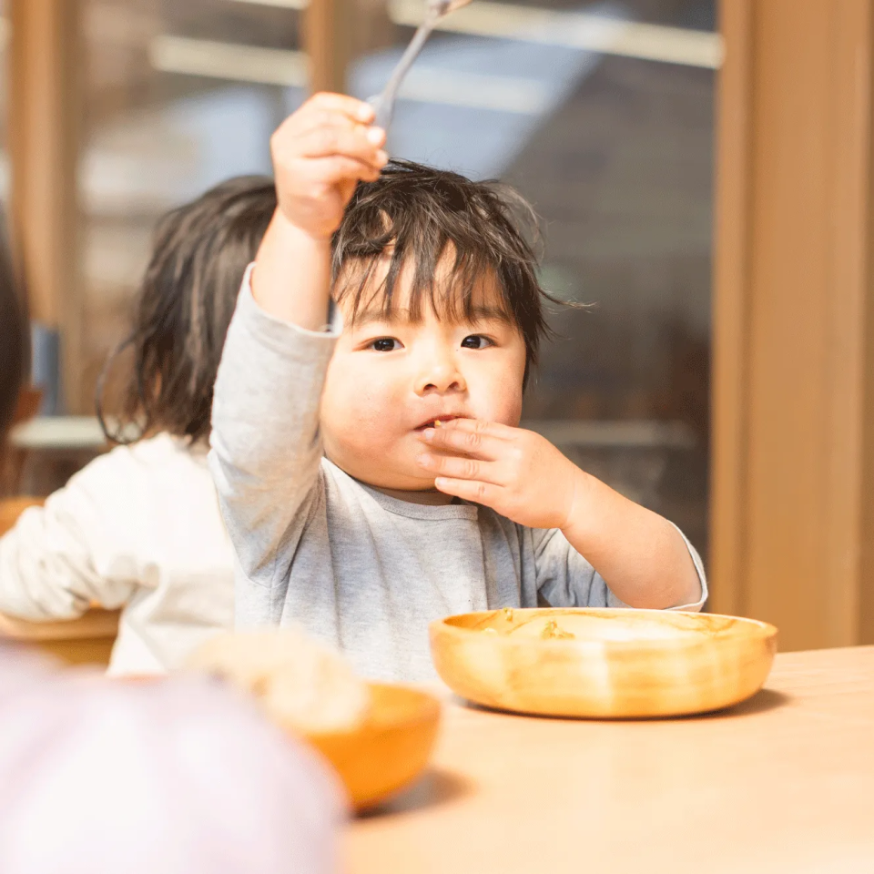 手を挙げてスプーンを持つ子ども