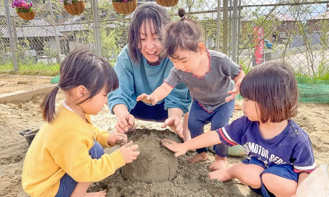 保育園の砂場で活動する先生と子どもたち